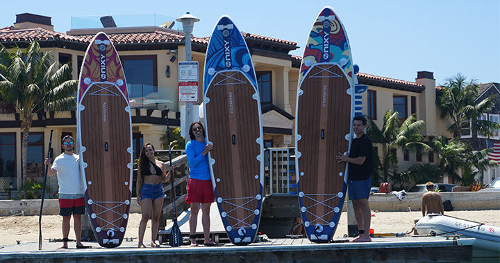 Lifestyle image of NIXY inflatable stand-up paddleboards in front of Newport Beach houses