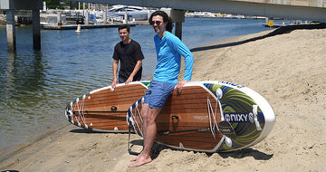 Two guys standing with their inflatable paddleboards on the sand