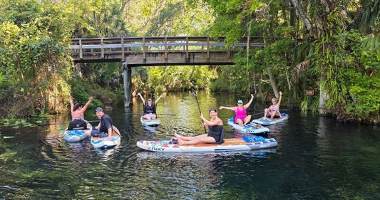 Family sitting on top of inflatable paddleboards in front of trees and a bridge