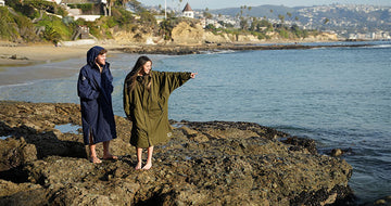 Man and women staying warm by wearing the NIXY Adventure Changing Parka at the beach 