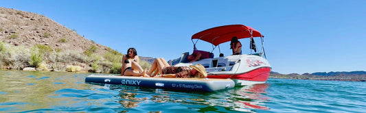 Women laying on a NIXY inflatable floating dock while on the water with a boat and scenic background.