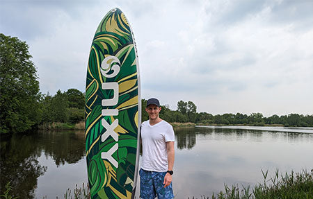 Man standing next to fully inflated paddleboard in front of a calm lake