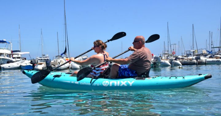 Man and women paddling on a NIXY Tahoe Inflatable Kayak (Aqua) on the water in front of boats