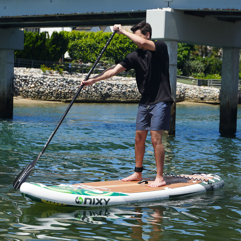 Man paddling a NIXY Newport G5 paddle board on a calm waterway under a bridge