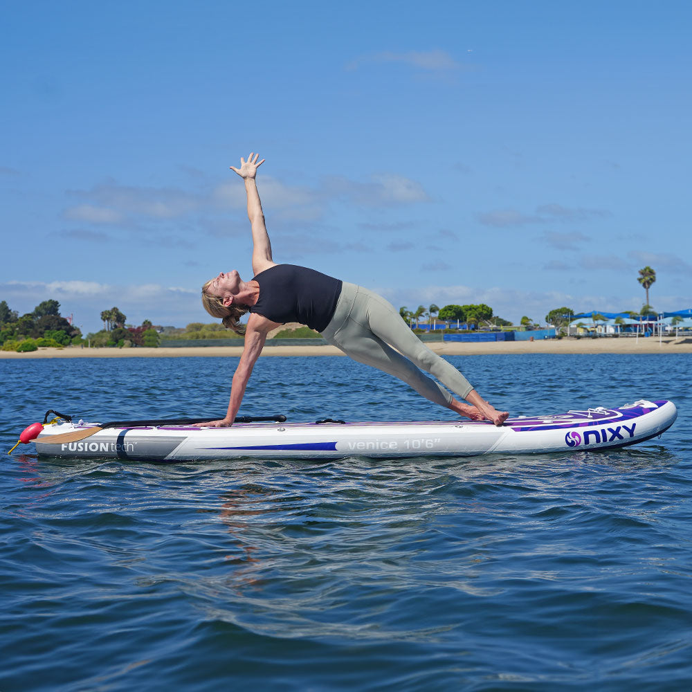 NIXY Venice G5 Yoga Paddleboard on the water while a women performs yoga poses.