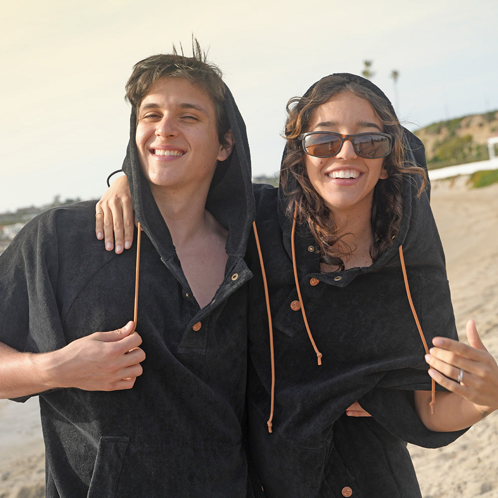 A man and woman wearing NIXY Changing Ponchos at the beach