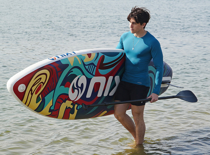 Man carrying NIXY Newport G5 inflatable stand-up paddleboard while walking in the water