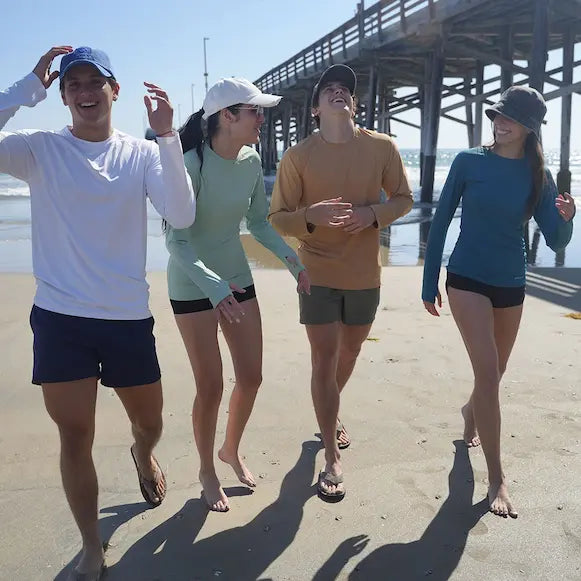 NIXY Rash Guard UPF 50+ Sun Protection worn by men and women while they walk on the sand in front of a pier