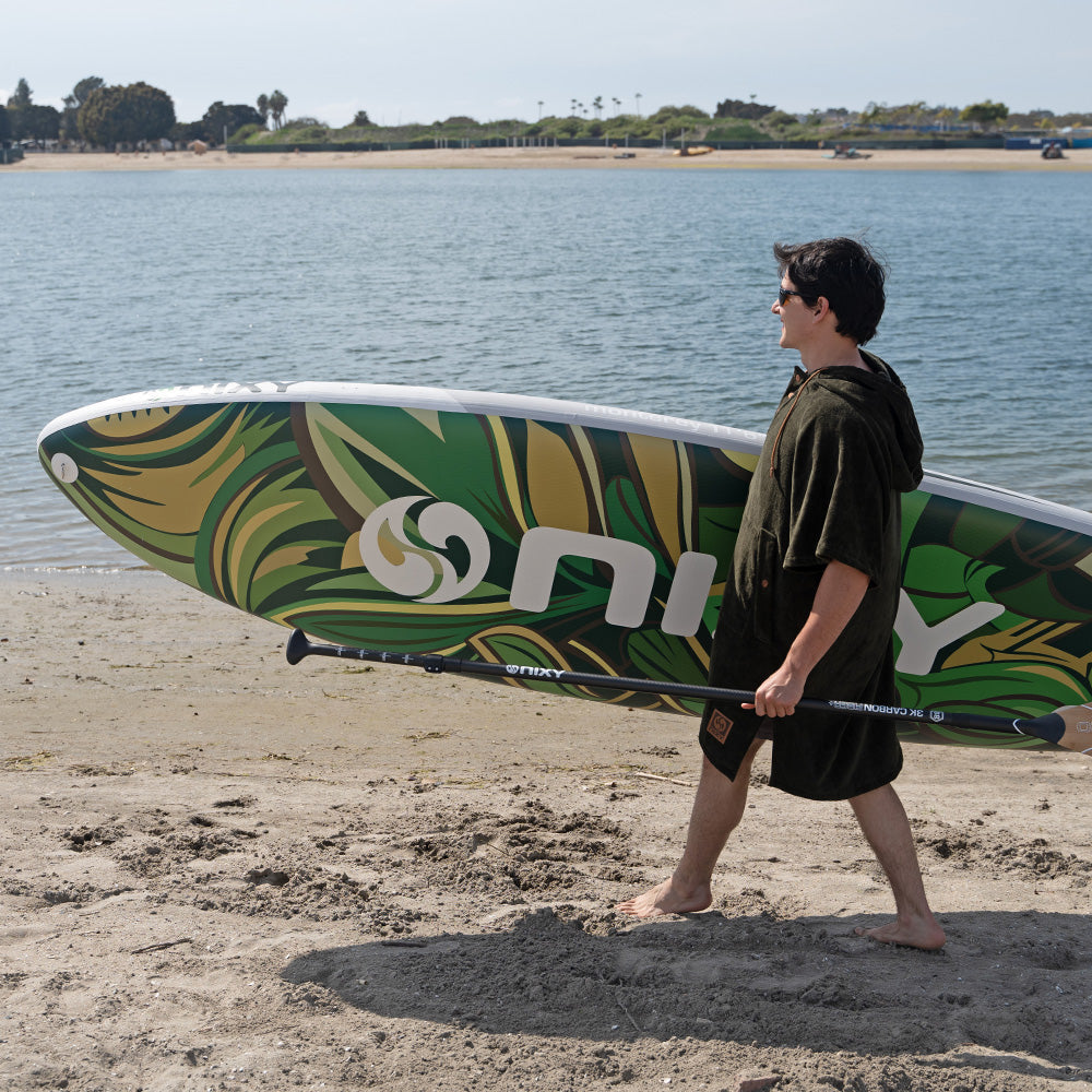 Man wearing a NIXY Changing Poncho while carrying an inflatable paddleboard