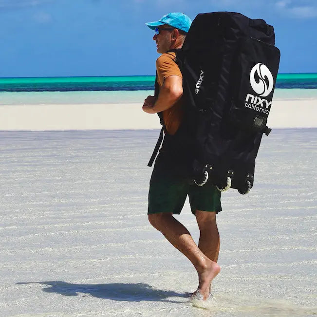 NIXY Three-wheeled Waterproof SUP backpack carried on a mans back while he walks on the shoreline