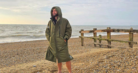 Man wearing waterproof and windproof adventure changing parka in front of a beautiful scenic beach