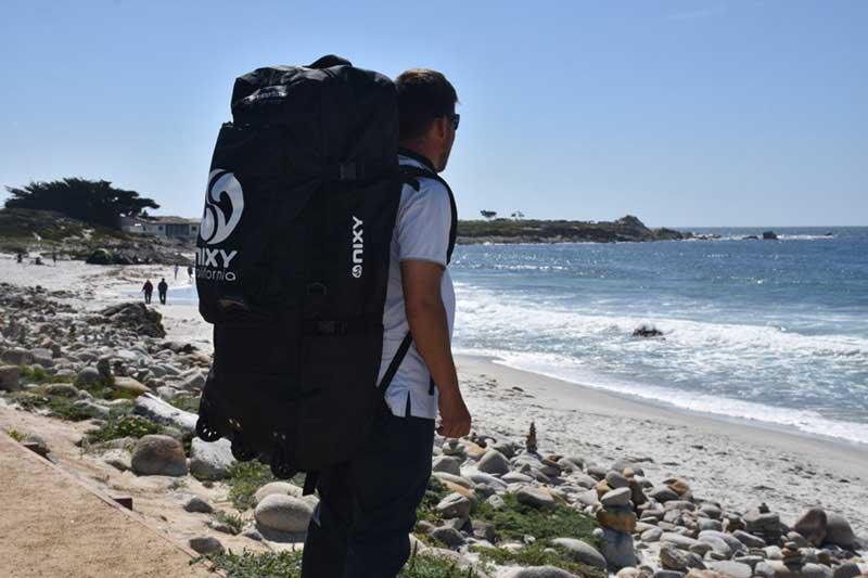 Man looking out into the water with an inflatable paddleboard on his back