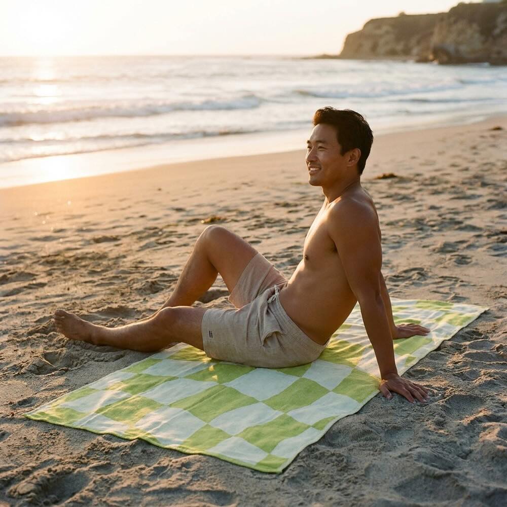 NIXY Turkish Cotton Beach Towel laid out on the sand while a man sits on top of it and stares at the ocean