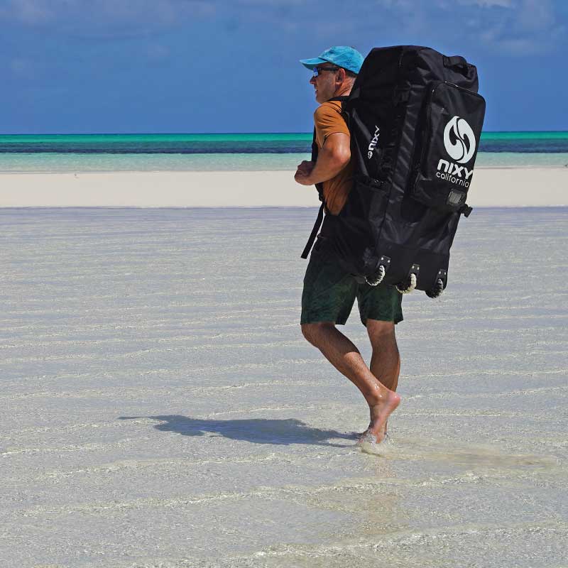 NIXY three-wheeled waterproof paddle board backpack carried across a sandy beach