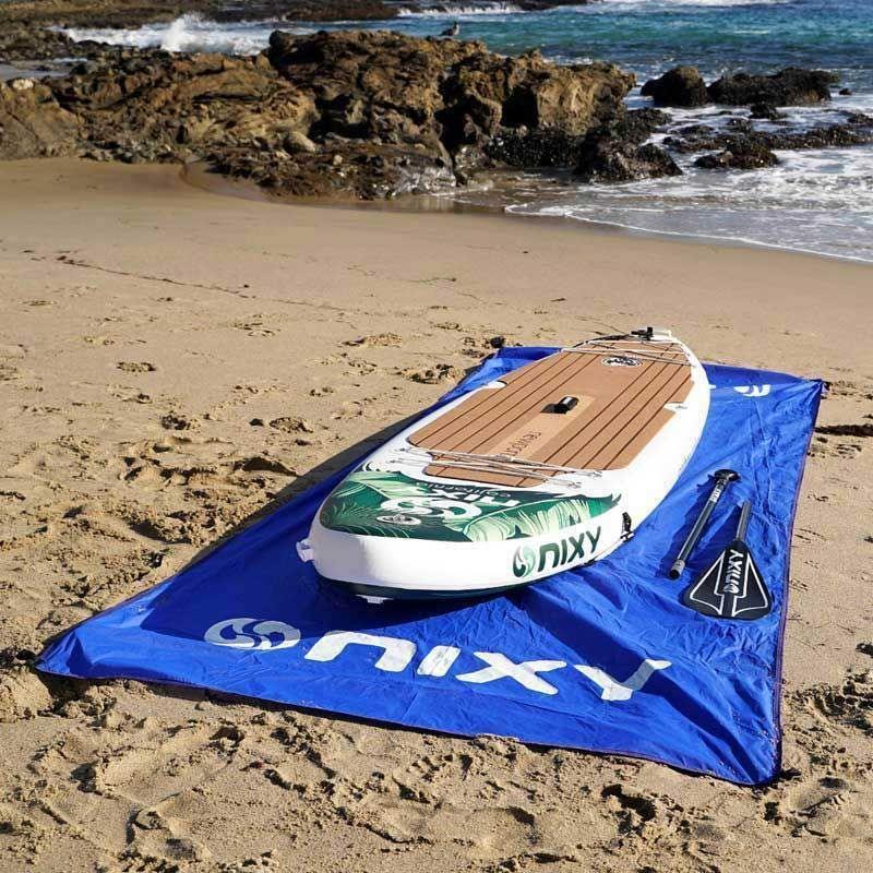 NIXY Landing Mat on a sandy beach with a NIXY inflatable paddle board and paddle resting on top
