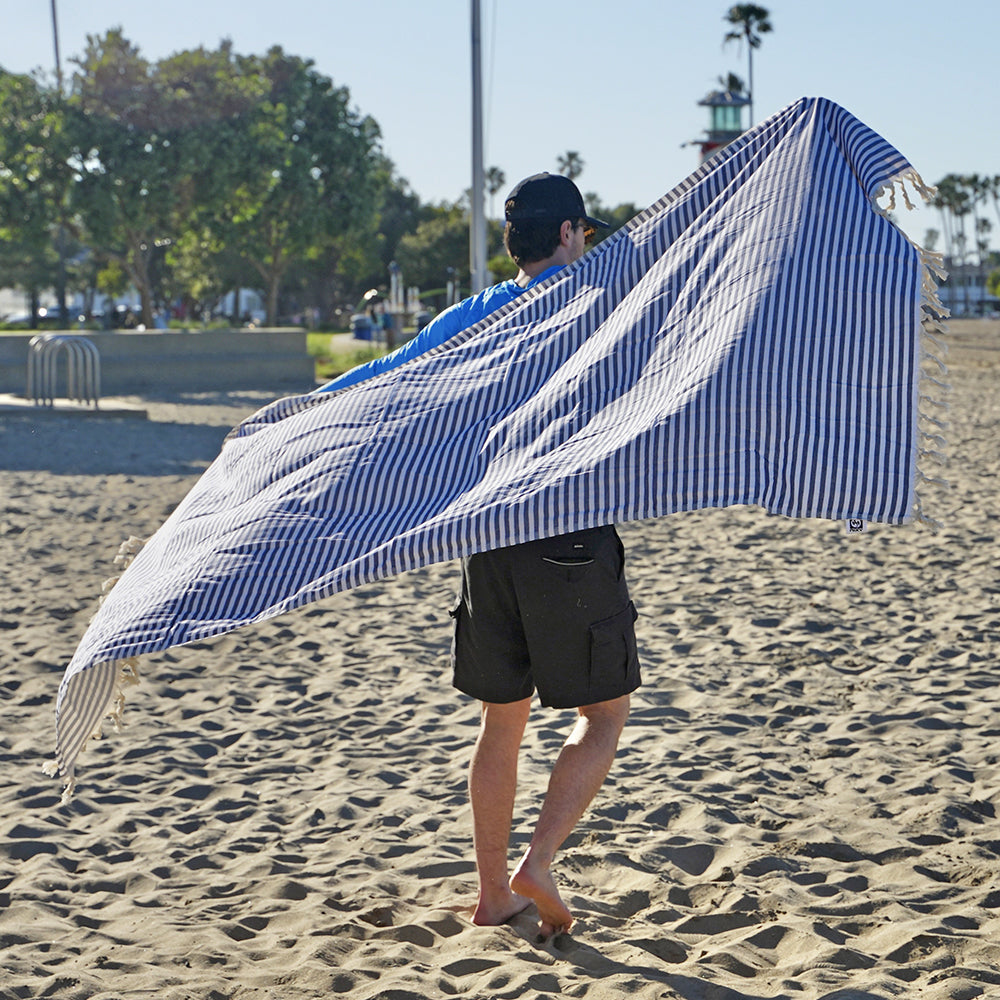 Person holding an extra large blue and white striped NIXY Mediterranean Turkish cotton beach towel on a sandy beach