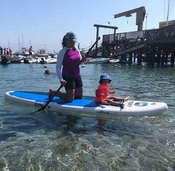Mom and child riding on top of a NIXY inflatable stand up paddleboard while on calm water