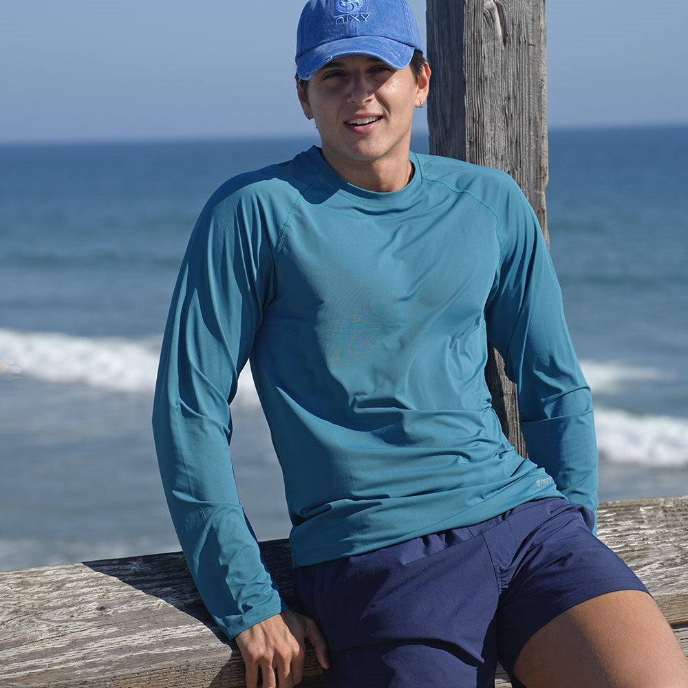 NIXY Rash Guard with UPF 50+ Sun Protection (Blue) worn by a man on a pier with the ocean behind him