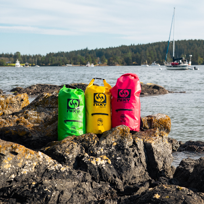 Three brightly colored waterproof dry bags with coastal scenery