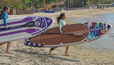 Women carrying inflatable stand up paddleboards to the water.