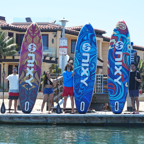 Four friends on a dock holding three NIXY Monterey G5 boards in Tulum, Exuma, and Ibiza prints