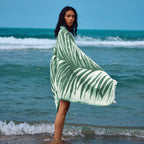 Woman standing on a beach wearing a green and white patterned towel.