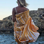 Person wrapped in a yellow and white patterned towel by the water