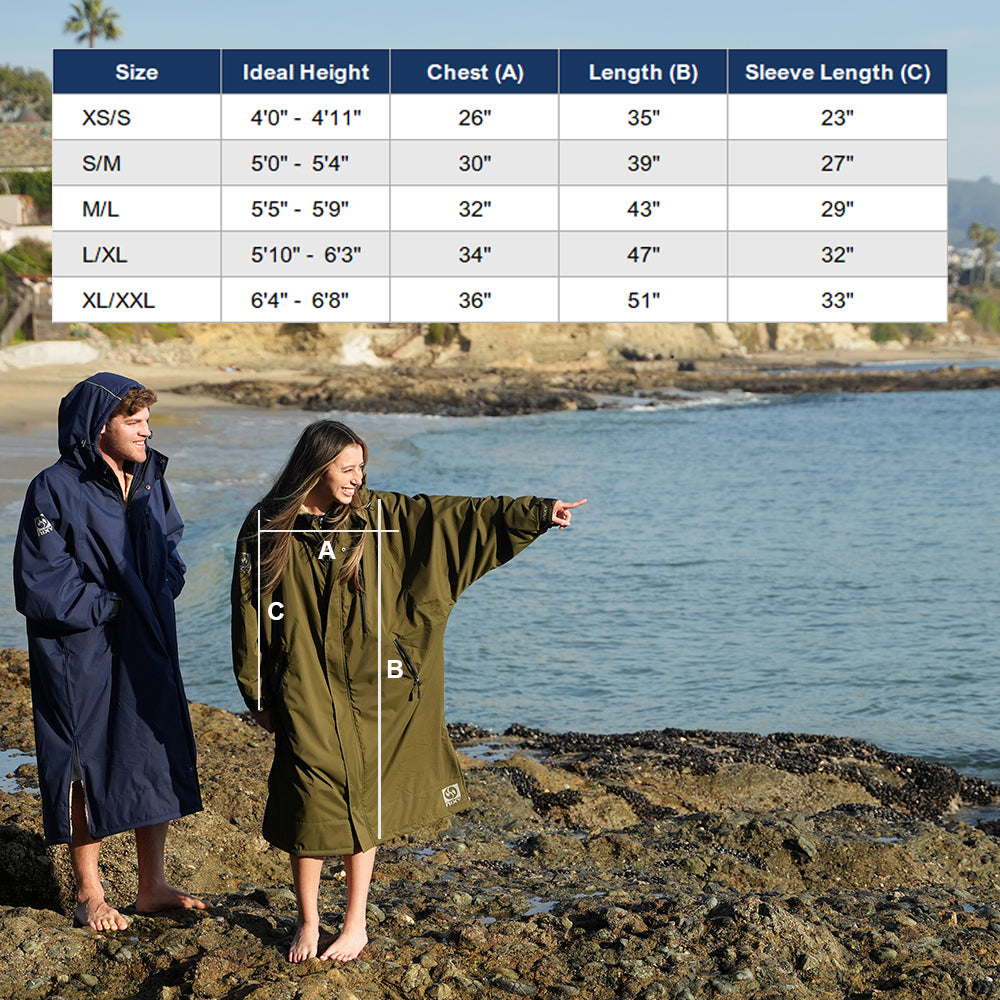 Two people wearing NIXY waterproof changing parka on a rocky beach with a size chart overlay.