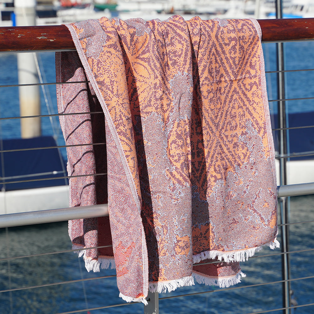 Patterned Turkish cotton beach towel draped over a railing with a marina background