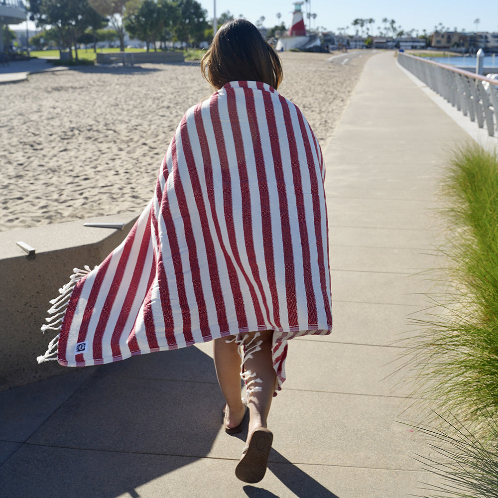 Person walking on a boardwalk with a red and white striped Turkish cotton beach towel draped over them