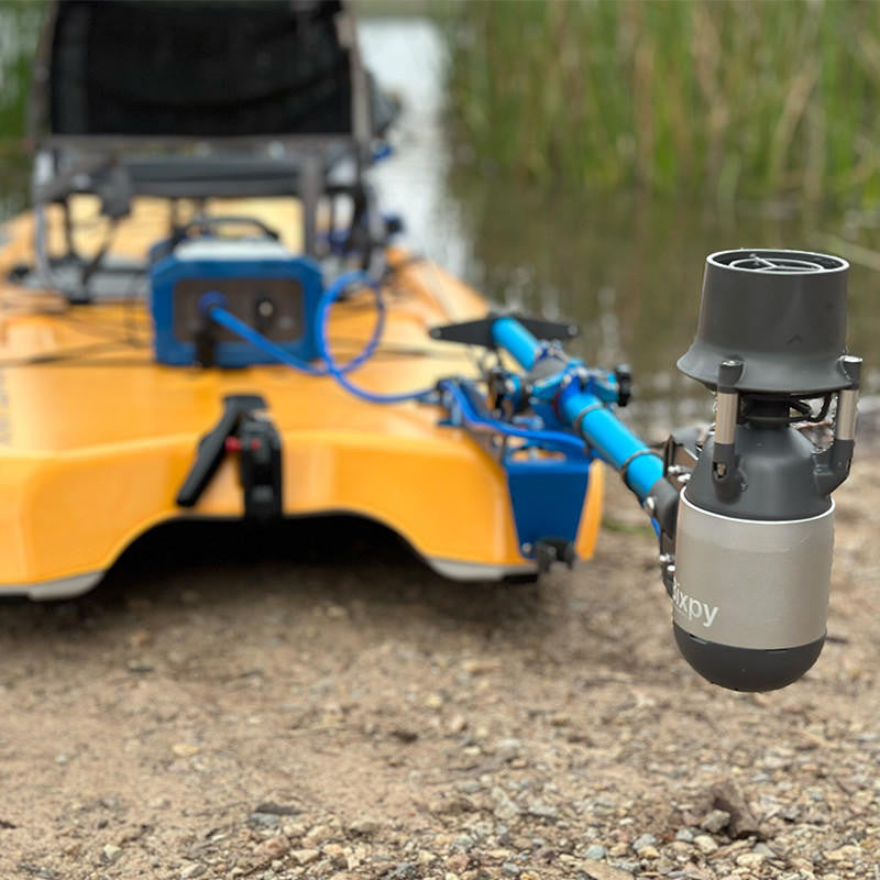 sit on top kayak with a motor and battery on a gravel shore near water.