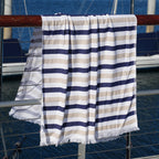 Striped Turkish cotton beach towel with blue and beige pattern draped over a railing with a boat in the background