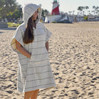 Person wearing a NIXY Turkish cotton adult changing poncho on a beach with a lighthouse in the background