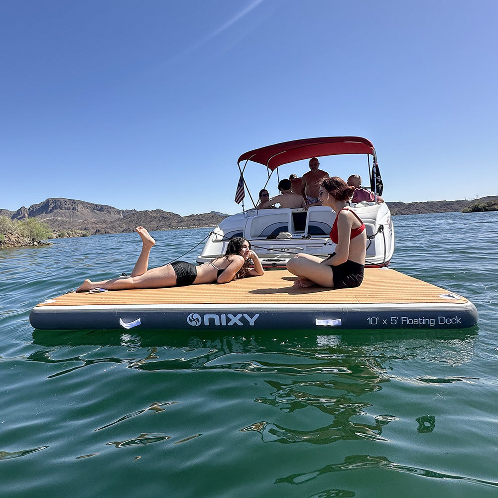 People relaxing on a NIXY floating deck in a lake with a boat in the background.