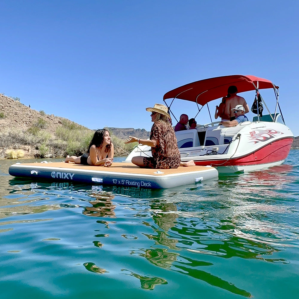 People on an inflatable deck and a motorboat on a clear blue lake with mountains in the background
