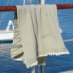 Green woven Turkish cotton beach towel hanging on a railing with water and boats in the background