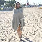 Woman wrapped in a striped Turkish cotton beach towel on a sandy beach with a lighthouse in the background