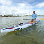 Man on a NIXY Malibu 14' Performance Inflatable Paddleboard on a calm body of water with a clear sky.