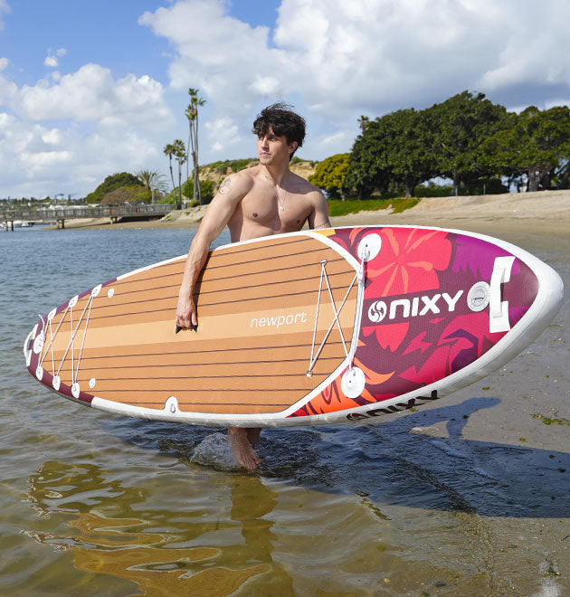 Man carrying a lightweight and durable NIXY G5 inflatable paddleboard while walking into the water