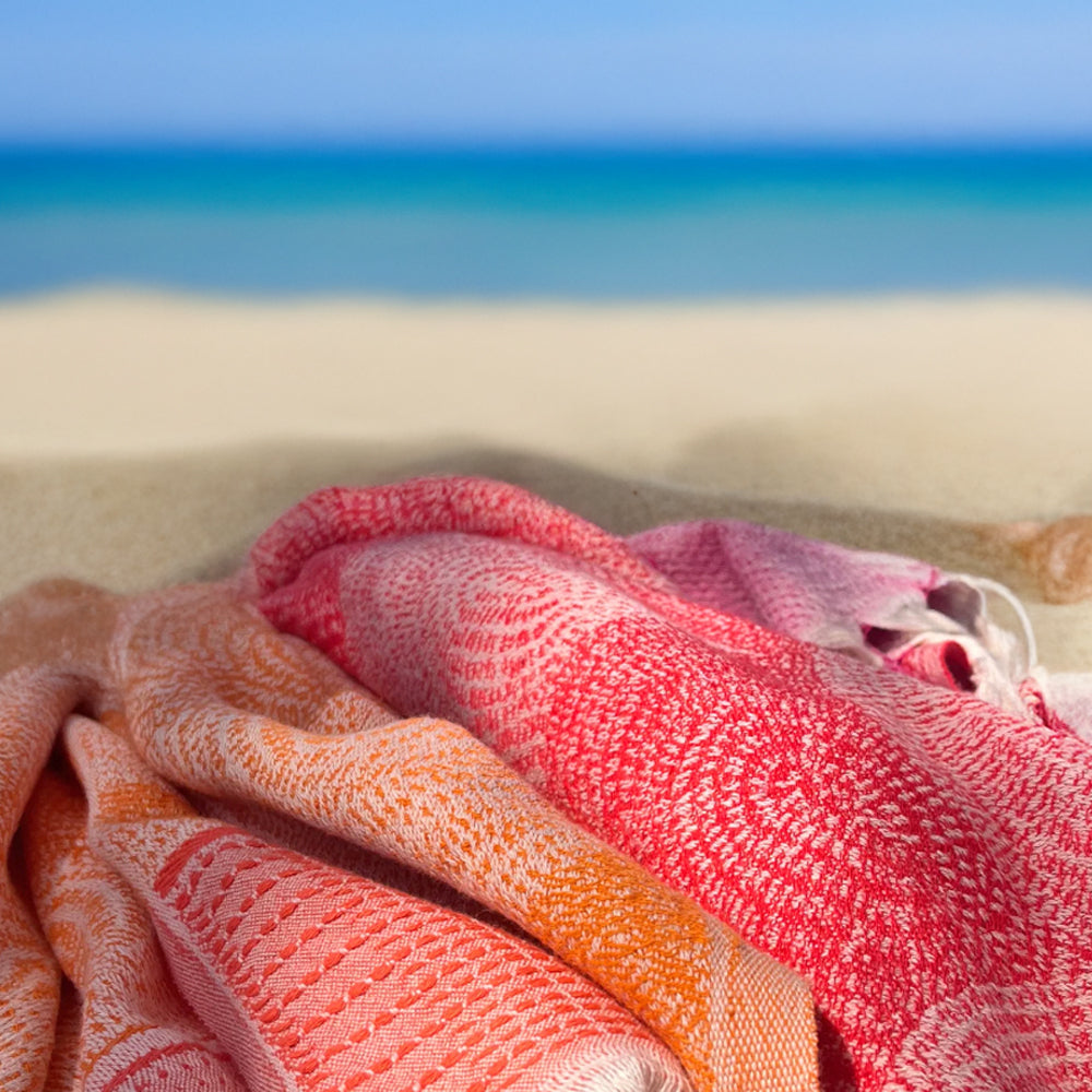 Folded beach towels in orange and pink on a sandy beach with ocean in the background