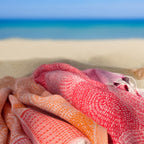 Folded beach towels in orange and pink on a sandy beach with ocean in the background