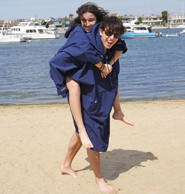 Man and women wearing surfing changing poncho at the beach